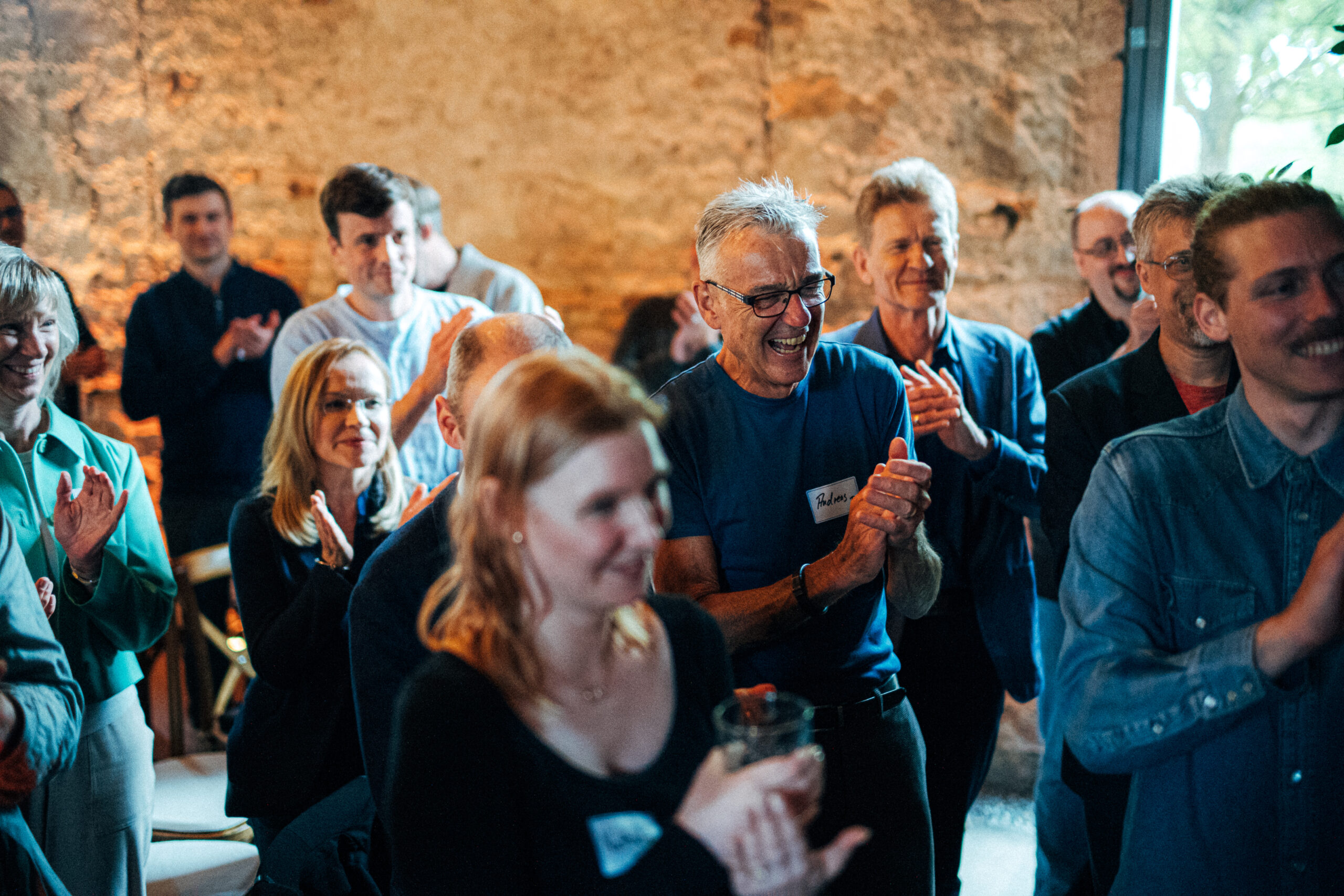 Mitarbeiter der HMS Analytical Software GmbH applaudieren bei einem internen Event in lockerer Atmosphäre vor Backsteinwand.
